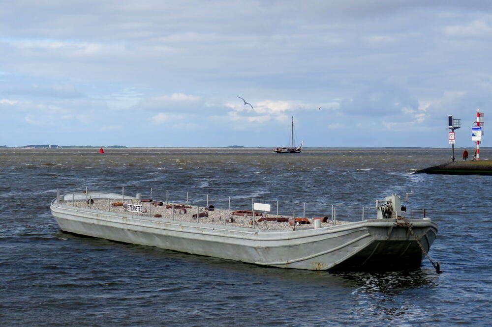 Een breed werkponton vaart langs het rood-witte havenhoofd de zeehaven van Lauwersoog binnen